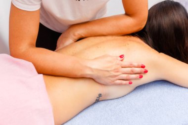 relaxed young woman lying face down on massage table enjoying therapeutic body massage by professional masseur in spa or wellness center.