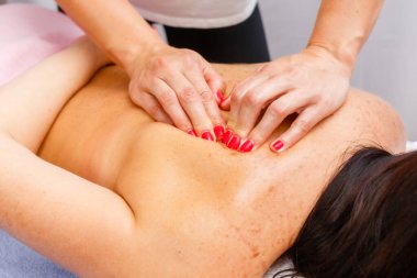 relaxed young woman lying face down on massage table enjoying therapeutic body massage by professional masseur in spa or wellness center.
