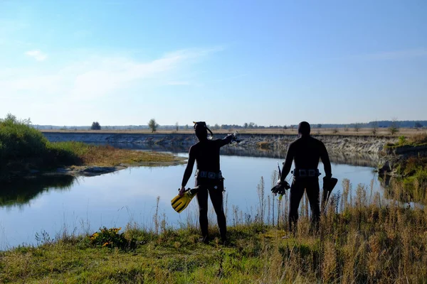 Two underwater hunters on the bank of the river are preparing to dive. Underwater fishing. Rear view