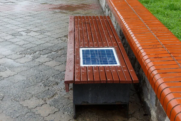 A bench with a built-in solar panel for charging phones. A place for charging gadgets and relaxing. New technologies in the city. The solar panel is built into the wooden bench.