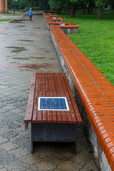 A bench with a built-in solar panel for charging phones. A place for charging gadgets and relaxing. New technologies in the city. The solar panel is built into the wooden bench.