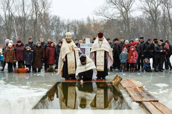 Ukraine, the city of Romny, January 19, 2013: A priest consecrates water with a cross in a cistern on the feast of the Baptism of the Lord. Orthodox rite of bathing in the ice hole. Epiphany