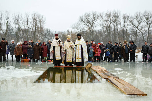 Ukraine, the city of Romny, January 19, 2013: A priest consecrates water with a cross in a cistern on the feast of the Baptism of the Lord. Orthodox rite of bathing in the ice hole. Epiphany