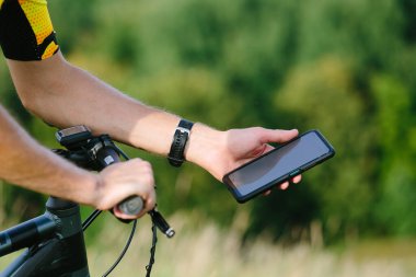 Happy male cyclist sending a text message on his mobile phone. Image of a cyclist on a mountain bike using a smartphone navigator, exploring a map and searching for GPS coordinates while cycling. Blurred image focus