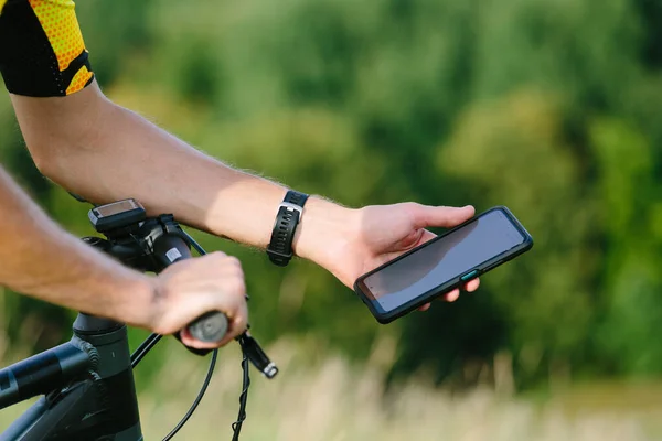 Happy male cyclist sending a text message on his mobile phone. Image of a cyclist on a mountain bike using a smartphone navigator, exploring a map and searching for GPS coordinates while cycling. Blurred image focus