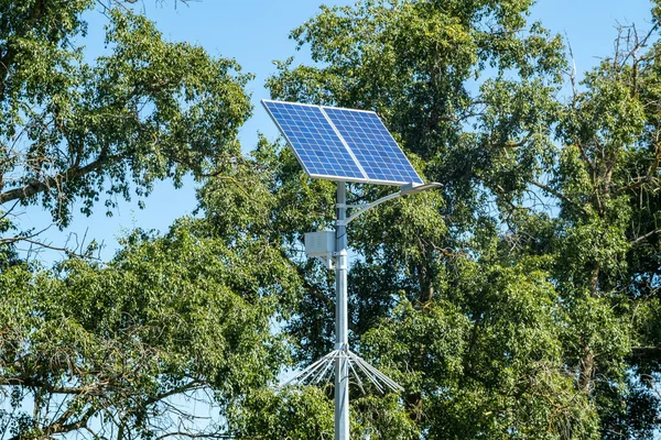 Lamp post with solar panel system on road with blue sky and trees. Autonomous street lighting using solar panels. Street lamp, on batteries from the sun. Alternative renewable energy systems on the street