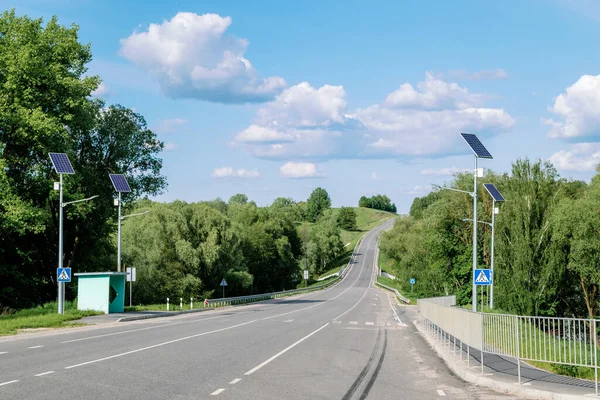 Lamp post with solar panel system on road with blue sky and trees. Autonomous street lighting using solar panels. Street lamp, on batteries from the sun. Alternative renewable energy systems on the street