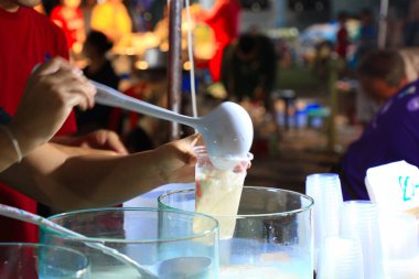 Meyve suyu tüccarı sokak yemeklerine su döküyor. Yaowarat sokak yemeği Tayland