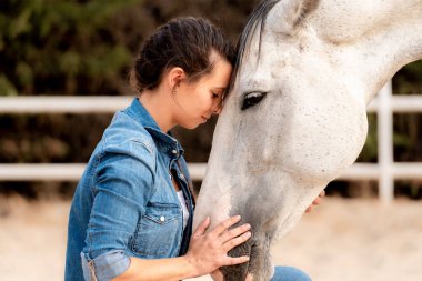 Side view of a woman with affectionate gesture to her horse grabbing her head with her head. High quality photo