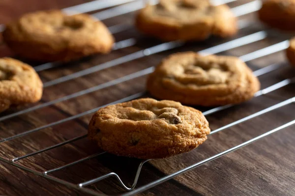 Chocolate chip cookies on a cooling rack on top of a dark wood background