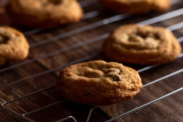 Chocolate chip cookies on a cooling rack on top of a dark wood background