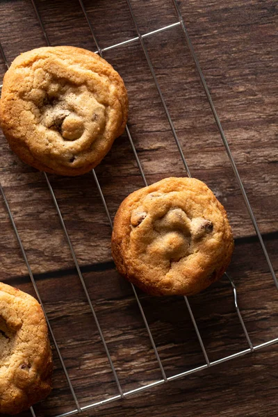 Chocolate chip cookies on a cooling rack on top of a dark wood background