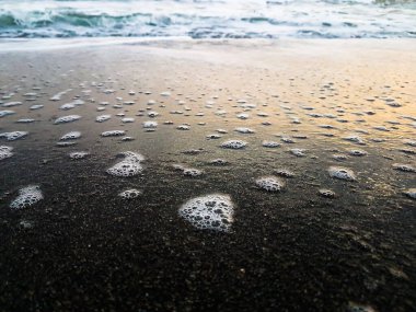 Deniz köpüğü kıyıya yeni düşmüştü. Bol miktarda deniz suyu barındıran ıslak kumu ve ondan çok güzel bir ışık yansıması görülebilir..