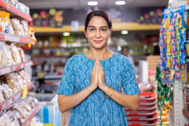 Portrait of an Indian woman greeting Namaste at grocery aisle of supermarket