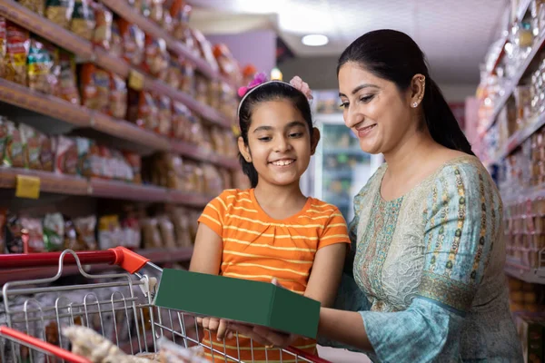 Mutlu anne ve kız süpermarkette alışveriş yaparken ürün bilgileri okuyor.