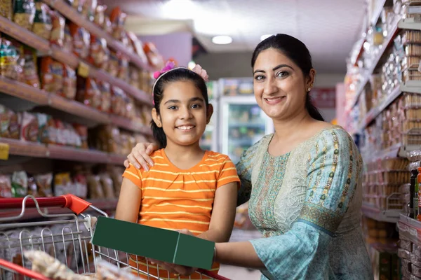 Mutlu anne ve kız süpermarkette alışveriş yaparken ürün bilgileri okuyor.