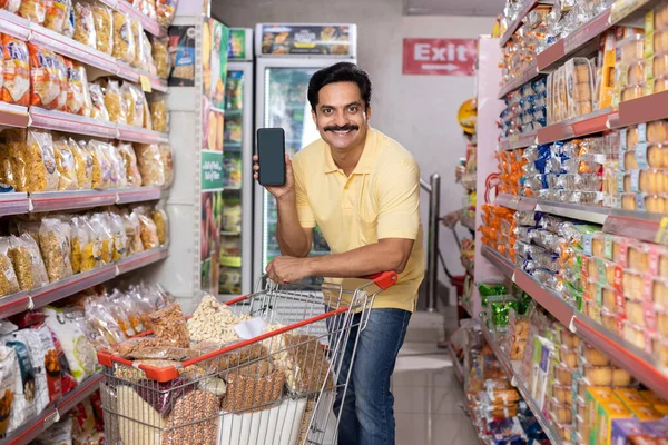 Markette boş bir cep telefonu ekranı gösteren mutlu adam.