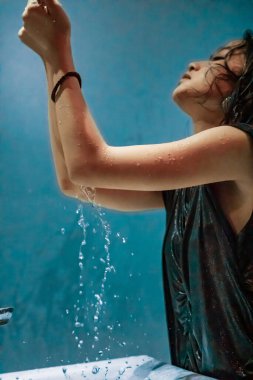 Asyalı kadınlar mavi banyodaki beyaz lavabodan elleriyle su alırlar.