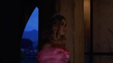 A Princess with a pink dress walking slowly in the dark while wearing a crown and tiara inside the castle