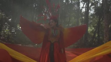 A Beautiful Chinese woman in a red bird costume with red and orange fabric in the background in the forest