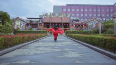 A beautiful Chinese woman running in the red costume inside the garden at the China Town