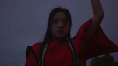 A Chinese Woman practicing a kung fu movement while standing on the mountain in the dark morning