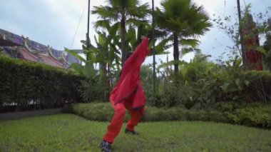 A Chinese Woman rehearsal a martial art performance inside the Chinese temple with the green bush in the background