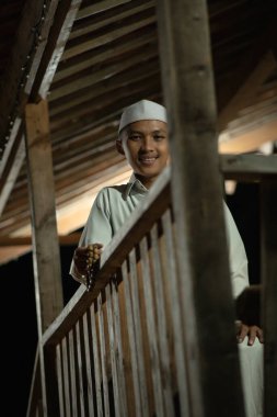 Karanlık bir gecede köyde beyaz bir Müslüman elbisesi giyerken balkonda dua eden İslami bir adam.