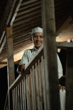 Karanlık bir gecede köyde beyaz bir Müslüman elbisesi giyerken balkonda dua eden İslami bir adam.