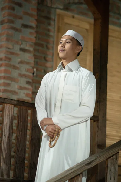 A Muslim man standing on the balcony of a wooden house in the village in the dark night