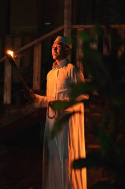 Elinde meşale olan Müslüman bir adam köyün önünde kamp alanının içinde duruyordu.