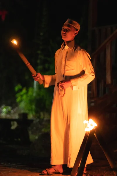 A Muslim man standing with the fire torch in her hand at the front of the village inside the campsite