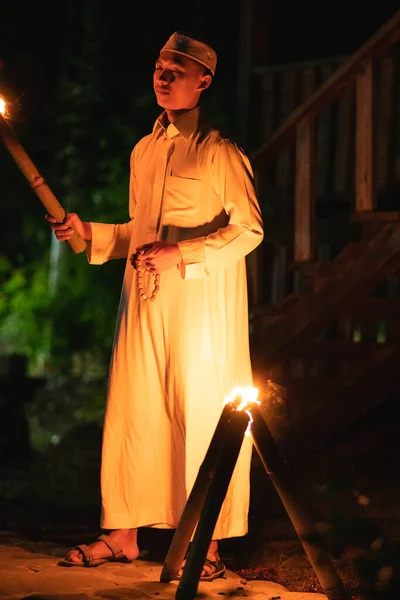 A Muslim man standing with the fire torch in her hand at the front of the village inside the campsite