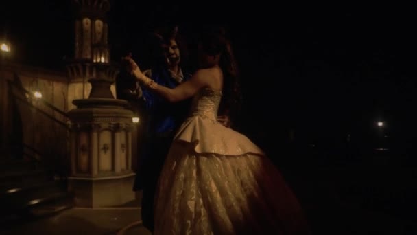 暗い夜に宮殿の前でドレスを着ている間に一緒にワルツを踊るカップル — ストック動画