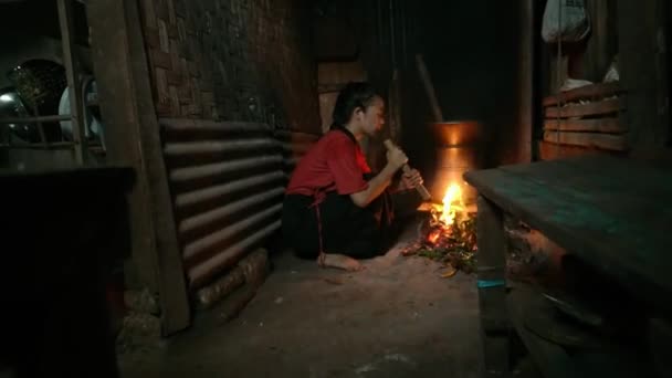 ブラインドアジアの女性古いキッチンで調理中に竹ブロワーの一片でヴィンテージの火ストーブを吹く — ストック動画