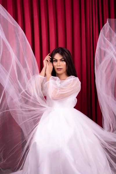 stock image Elegance Asian woman wearing a wedding dress with flying fabric around her in front of the red curtain inside the studio