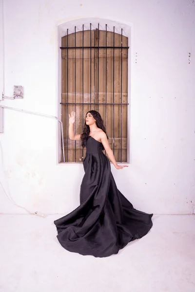Sad Asian woman standing in front of the brown wooden window while wearing a black dress inside the studio