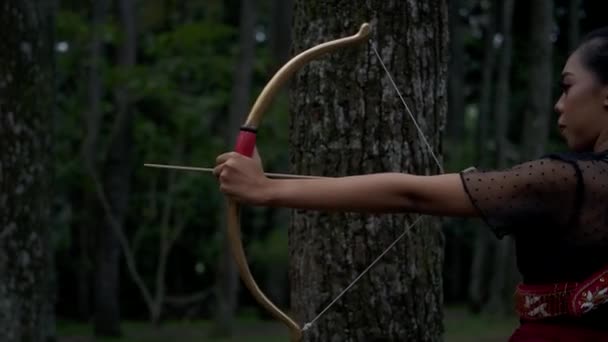 アジアの女性は ジャングルの中で黒のドレスと黒の長い髪で勇敢に立って弓から矢を撃つ準備ができて — ストック動画