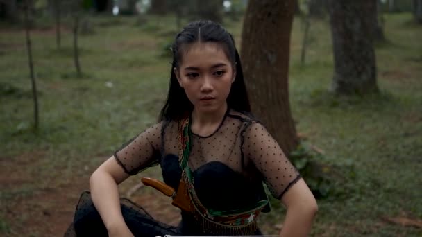 亚洲女人穿着黑色服装 留着黑色长发 坐在树间 手里拿着箭在森林里寻找猎物 — 图库视频影像