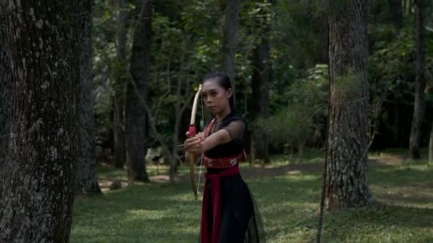 ジャングルの金の弓から矢を撃つ準備ができている女性の手のショットを閉じる — ストック動画