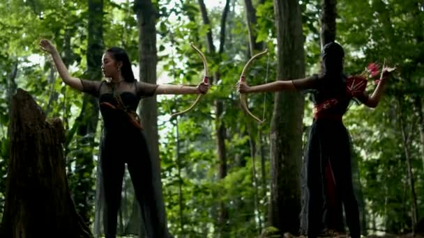 アジアの二人の女性が矢を引いて 森の中で敵を撃つ準備の弓に矢を置きます — ストック動画