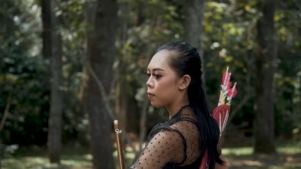 弓と矢を手にジャングルの中で敵を追いかける射手の女性 彼女は彼女の体に黒い衣装で地面に狩り — ストック動画