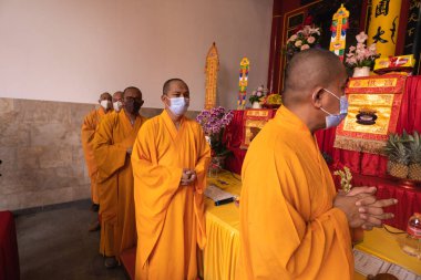 Bandung, Endonezya - 8 Ocak 2022: Turuncu ve kırmızı cüppeli bir grup keşiş Buda tapınağının mihrabında birlikte dua ediyorlar.