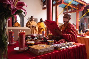 Bandung, Endonezya - 8 Ocak 2022: Turuncu ve kırmızı cüppeli bir grup keşiş Buda tapınağının mihrabında birlikte dua ediyorlar.