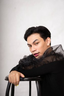 Güzel Asyalı adam elini ve kafasını sandalyenin üstüne koyup stüdyoda siyah bir elbise giymişti.