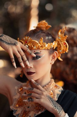 Kafasına ve boynuna altın aksesuarlar takmış, cesur makyajlı egzotik bir kadın ormanda siyah bir elbise giyiyordu.