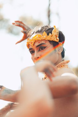 Asyalı bir adam yüzünde altın bir taç olan makyajla ormanın içinde poz verirken sinirli görünür.