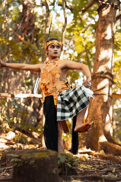 An angry Asian man poses shirtless while wearing a gold crown with stripped pants inside the forest