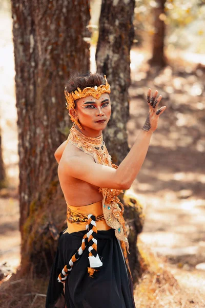 Manly Asian man posing in a golden crown and golden clothes while wearing makeup inside the forest