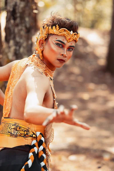Manly Asian man posing in a golden crown and golden clothes while wearing makeup inside the forest